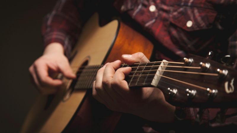 pessoa tocando violão para trazer a ideia de ritmo e musicalidade